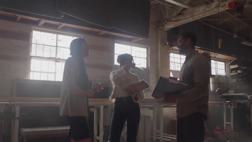 Three people talk in industrial space with barred windows and equipment in background