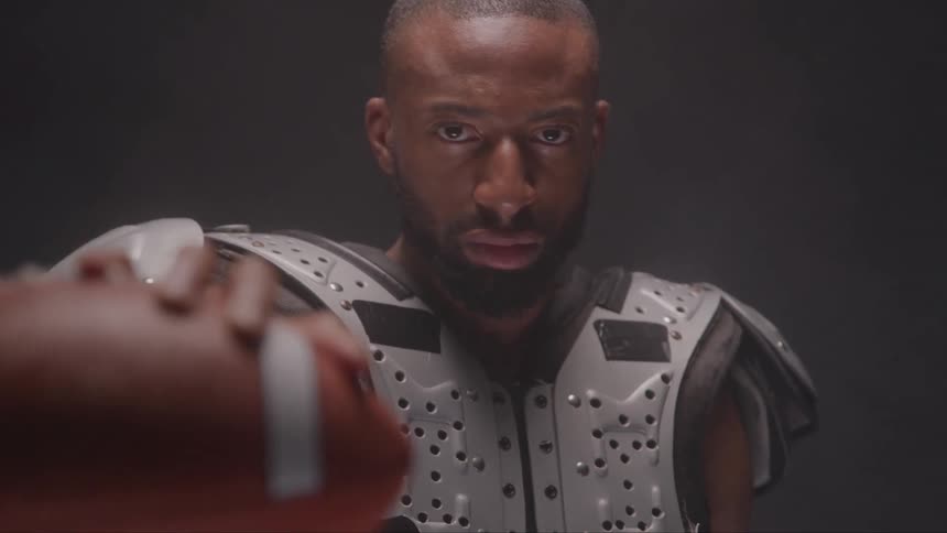 Person holds american football with serious expression in a dark smoky setting