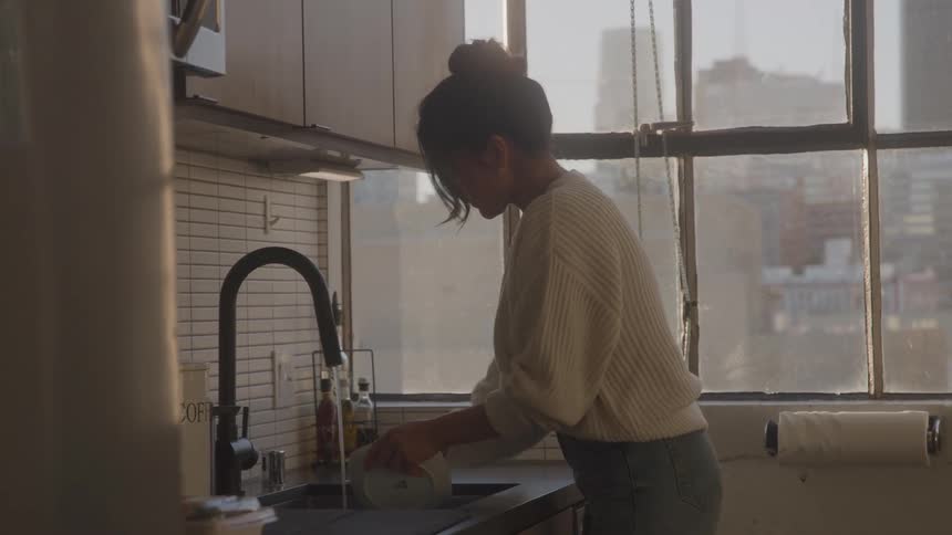 Person washes utensils at a modern kitchen sink with urban view