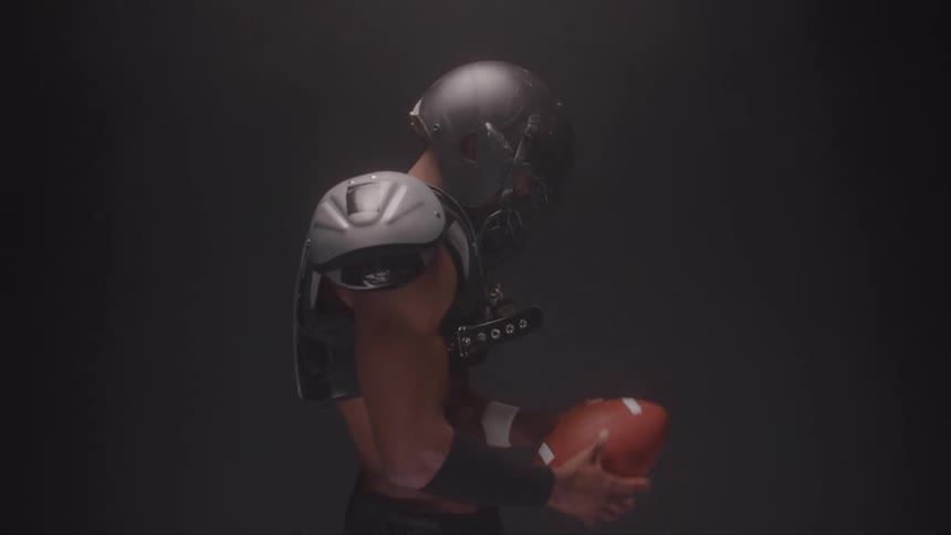 American football player holds ball with both hands in dark smoky setting