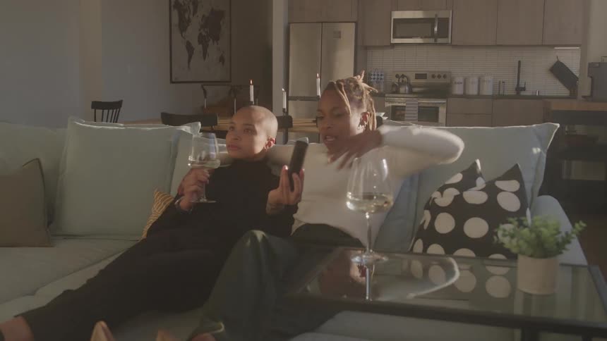 A young black couple sitting together on a couch while drinking and watching television in a living room during daytime