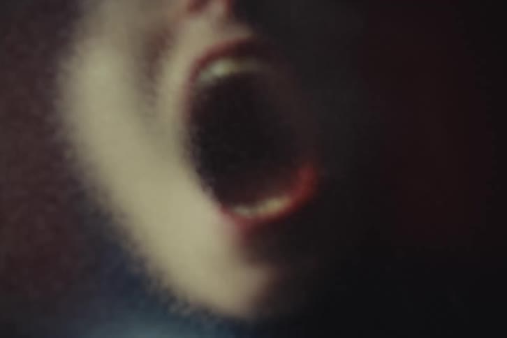 Open mouth in intense expression appears blurred in a dark grainy setting