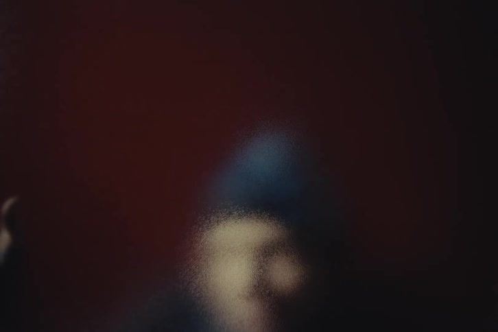 Blurred figure with hands pressed against translucent surface in a dark reddish setting