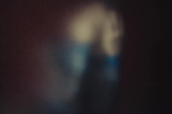 Blurred figure behind fogged glass gently raises a hand
