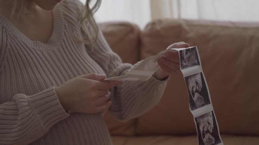 A pregnant woman smiles while tenderly looking at a strip of ultrasound images