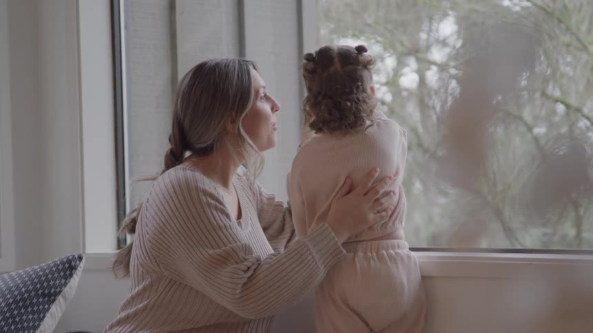 Adult holding child while looking out at the wooded outdoor area through the window