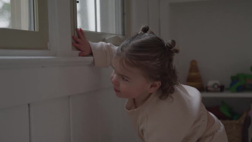 The little girl climbs up to look out the window