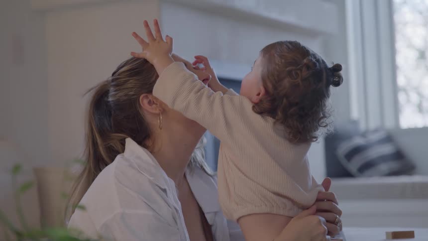 A mother and her toddler embrace and play a cute game of stacking blocks on the mothers forehead laughing together in a brightly lit room