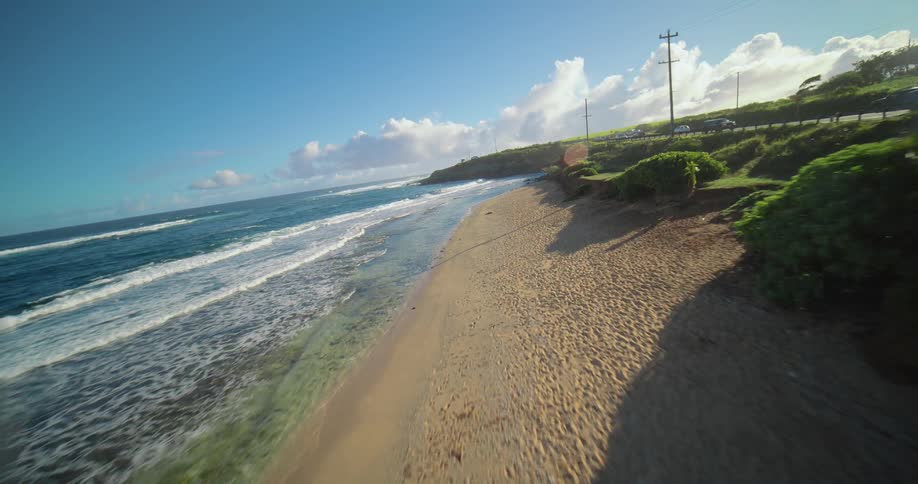Coastal road winds alongside the blue sea and sunlit green fields
