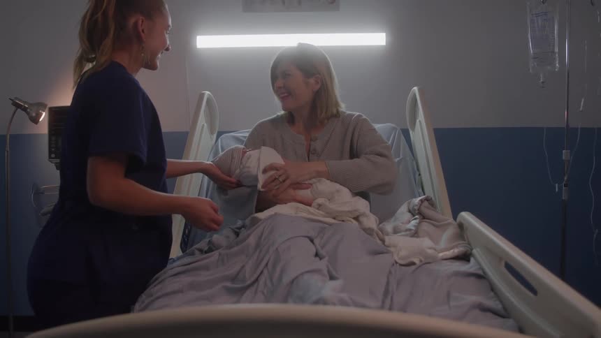 Nurse handing newborn to new mother sitting in a hospital bed