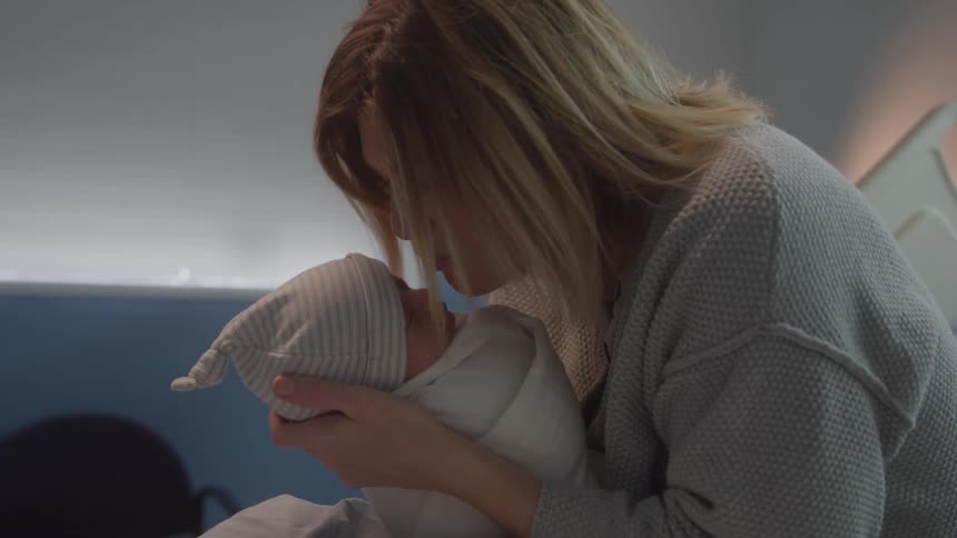 Mother looks at the newborn in her arms with care and attention