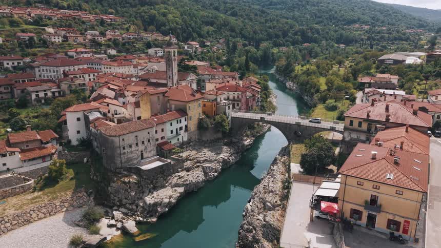 Historic town with reddish rooftops stretches along a river surrounded by green hills