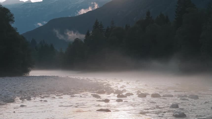 Soft mist hovers over the river at dawn in the mountains