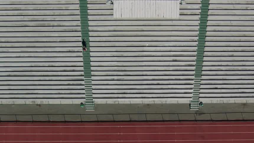 A man runs up the steep steps of empty bleachers next to red running track