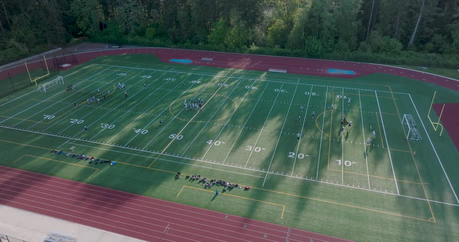 High school students run drills during lacrosse practice on a mixed use athletic field bathed in late afternoon light