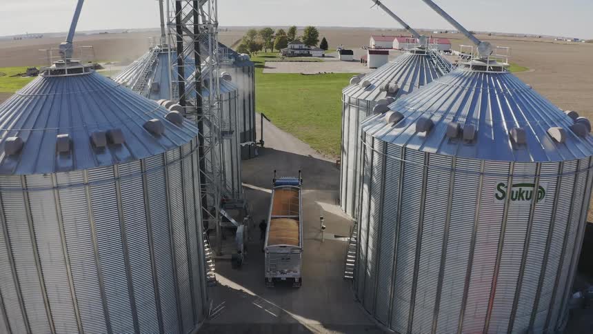 The truck has a trailer full of grain near the silos