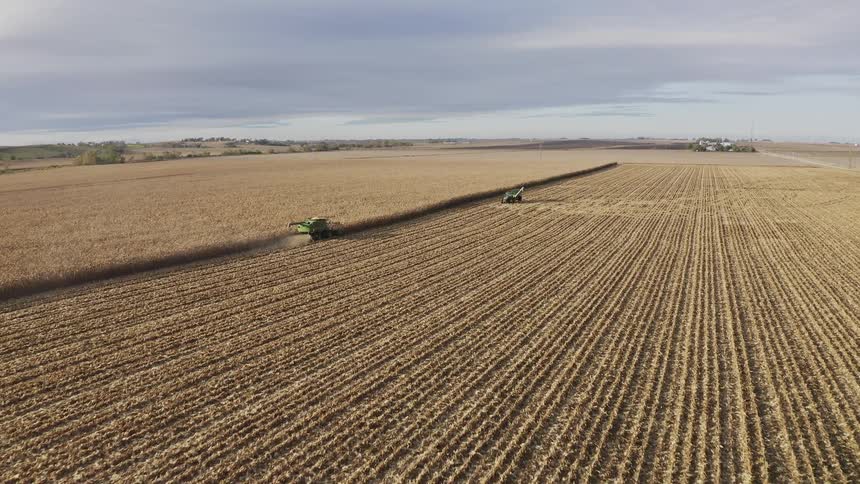 Aerial of a farm vehicle harvesting and clearing crops on a farm field during daytime