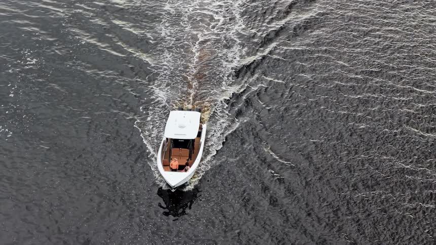 A small white motorboat carves a vshaped wake across dark rippling water with a couple of passengers onboard