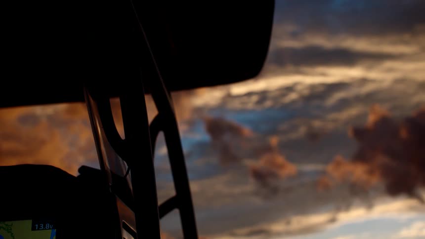 A view from inside a cockpit shows the silhouette of the windshield frame against a dramatic sky with golden and dark clouds at sunset or sunrise