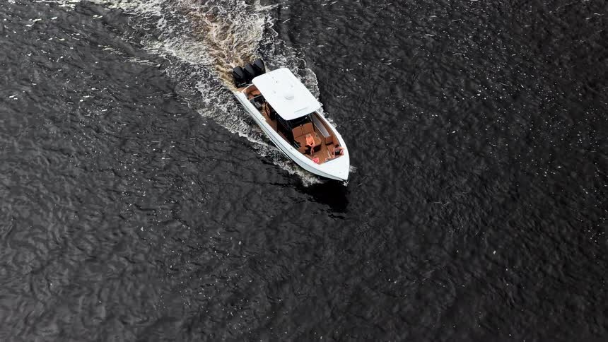 White boat cuts through dark waters leaving a trail of foam behind