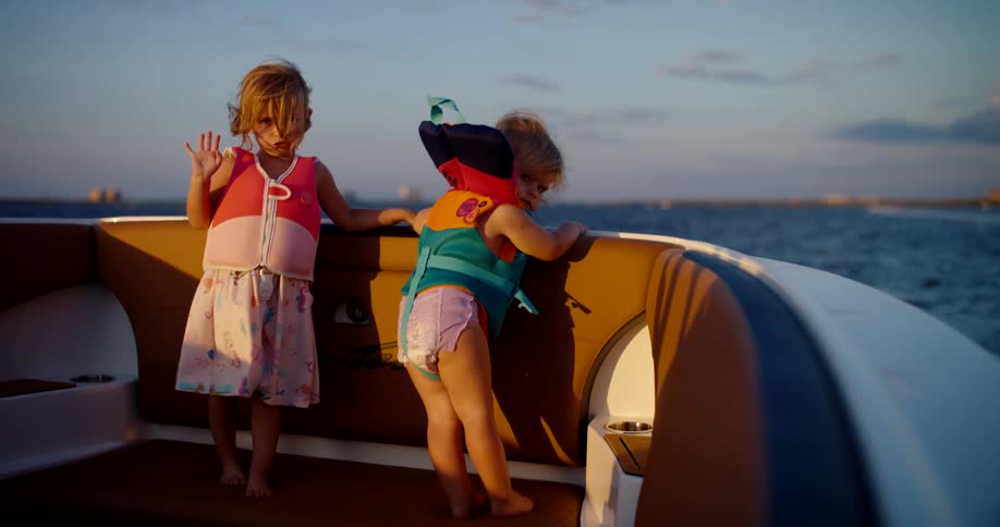 Children in life jackets playing on boat during sunset over calm waters