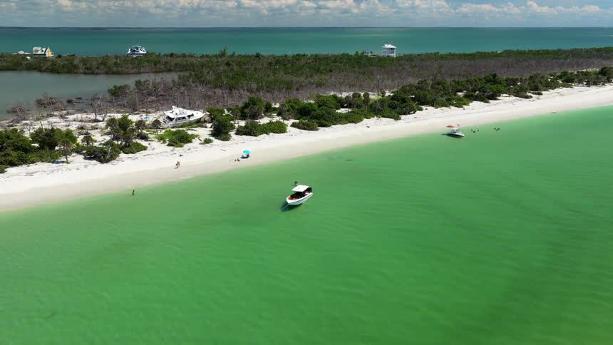 Boats anchored near a beach with green waters and light sand on a sunny day
