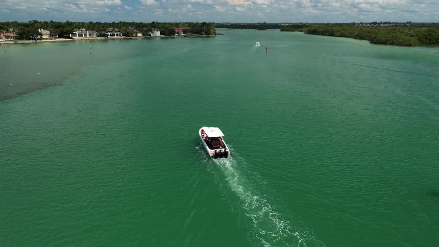 Motorboat cruising through green waters toward shoreline with houses and trees in the background