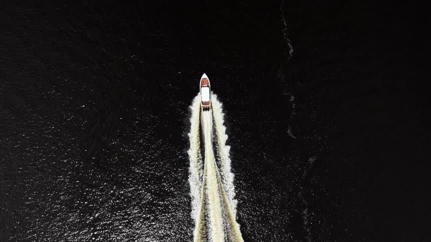 Speedboat cuts through dark waters at high speed leaving a long trail of foam