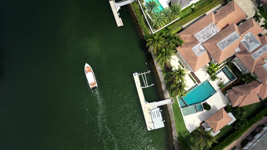 Boat sails near luxurious houses with pools by the water