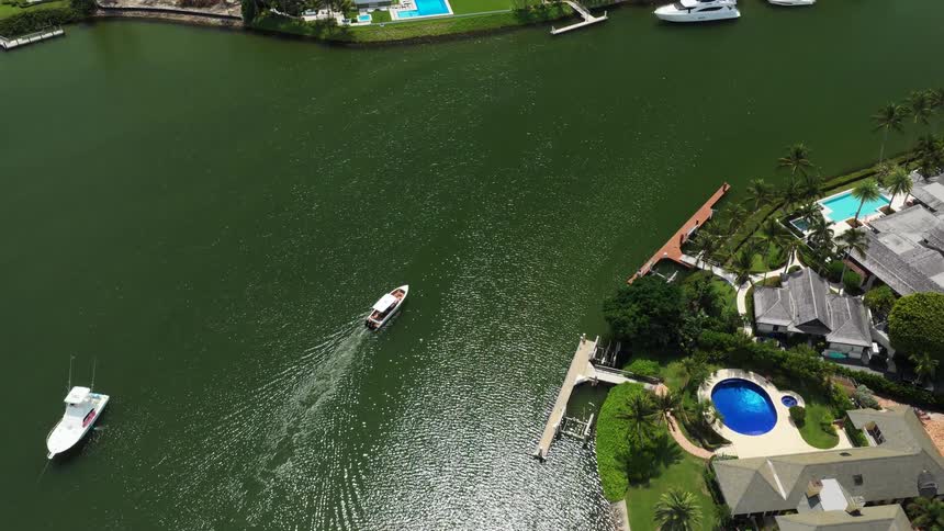 Boats navigate through a canal surrounded by houses and pools in a residential area