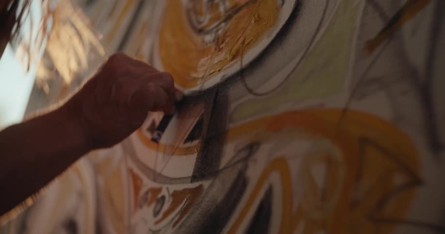 Hand draws details on an abstract painting in shades of yellow and brown