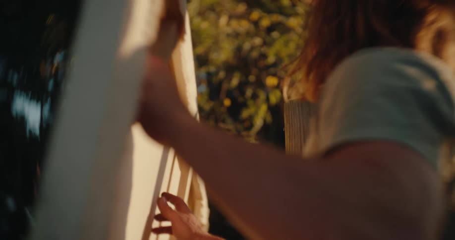Person wearing a hat holds a canvas while working outdoors at sunset
