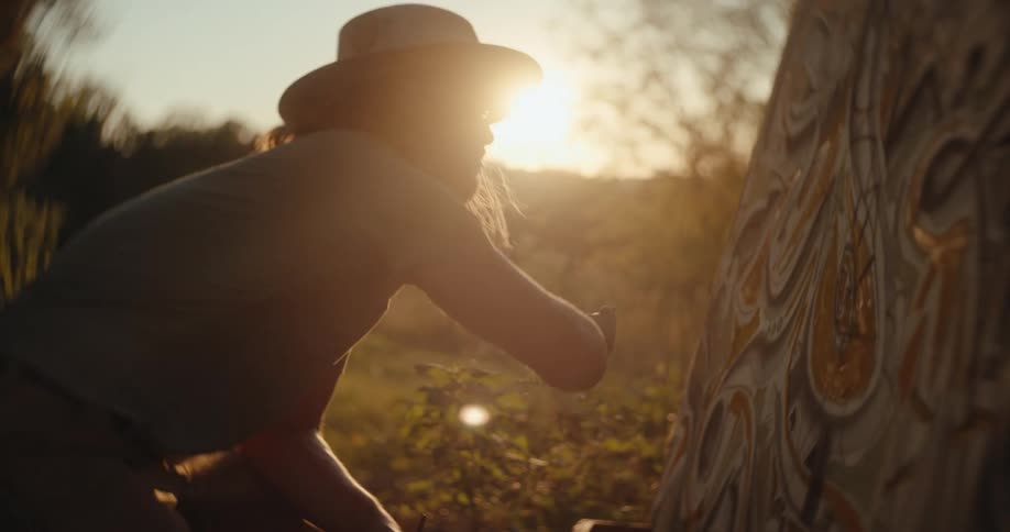 Artist paints a canvas outdoors under the golden light of sunset
