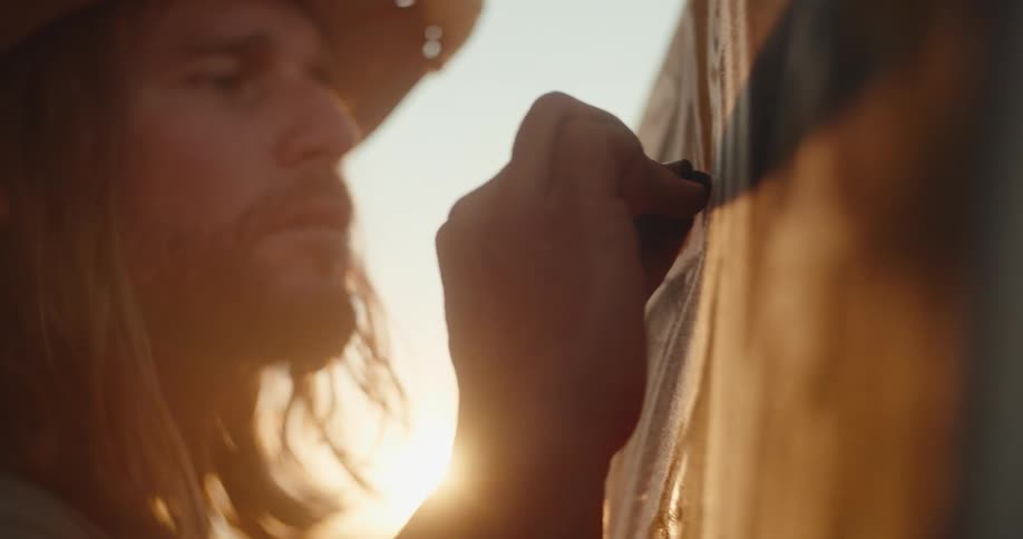 A man is writing on a board using chalk under bright sunlight