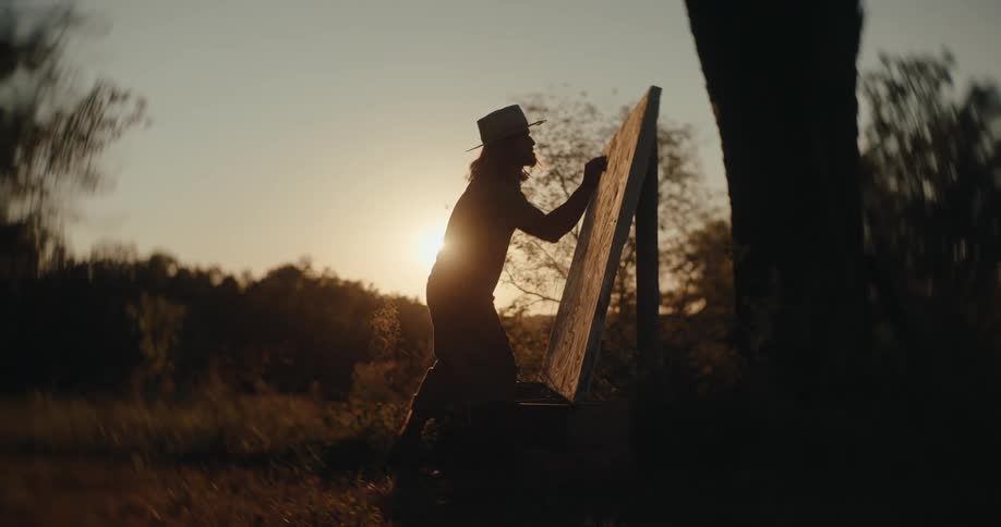 Person paints on an easel outdoors during sunset