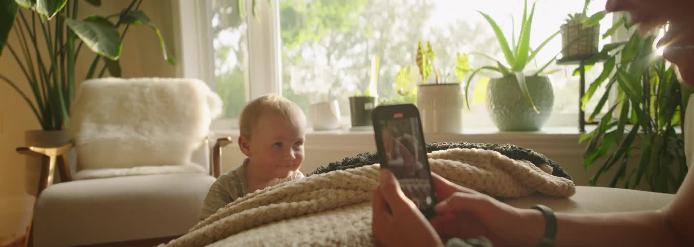 Mother records her son on video in the living room surrounded by plants