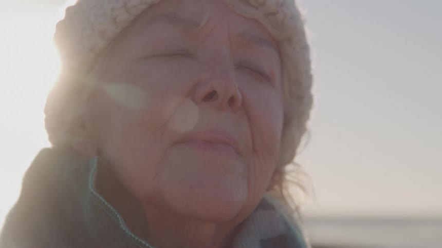 Elderly woman with closed eyes feels the sunlight on her face on a clear day