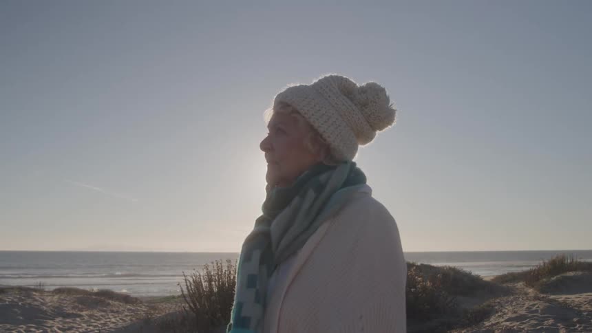 Elderly woman wearing a hat and scarf enjoys the sea view on a sunny day