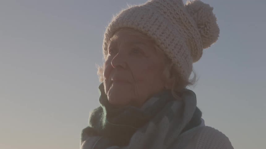 Elderly woman wearing a hat and scarf admires the landscape under the soft evening light