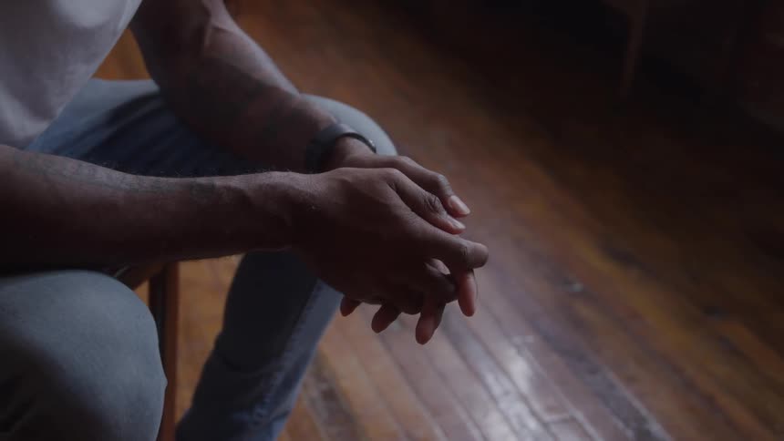Close up of a man sitting and clasping his hands indoors