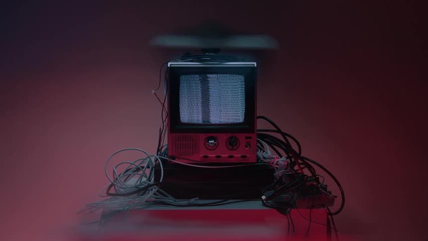 Small television screen displays signal static while sitting on a media player surrounded by cables