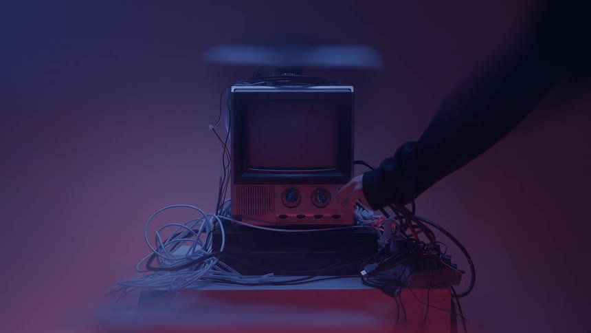 Hand turns a knob while turning off an old television surrounded by cables