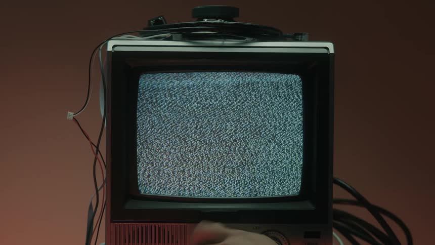 The person turns the knob trying to get rid of the static on the television