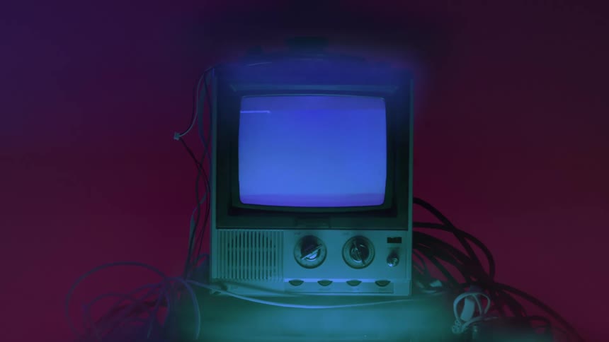 A retrostyle television set displaying a bluetinted image surrounded by loose cables illuminated by contrasting blue light from above and a red light from the background