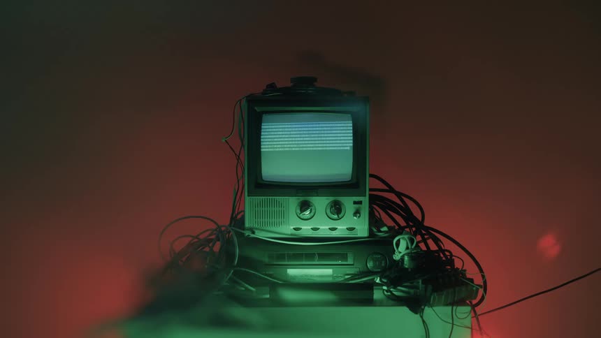 This video shows a vintage black and white television set sitting on top of another piece of electronic equipment possibly a vcr or receiver the tv screen displays horizontal static linesthe scene is moody and dimly lit with a strong red an