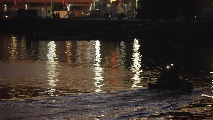 Boat with several people glides across the water reflecting the citys night lights