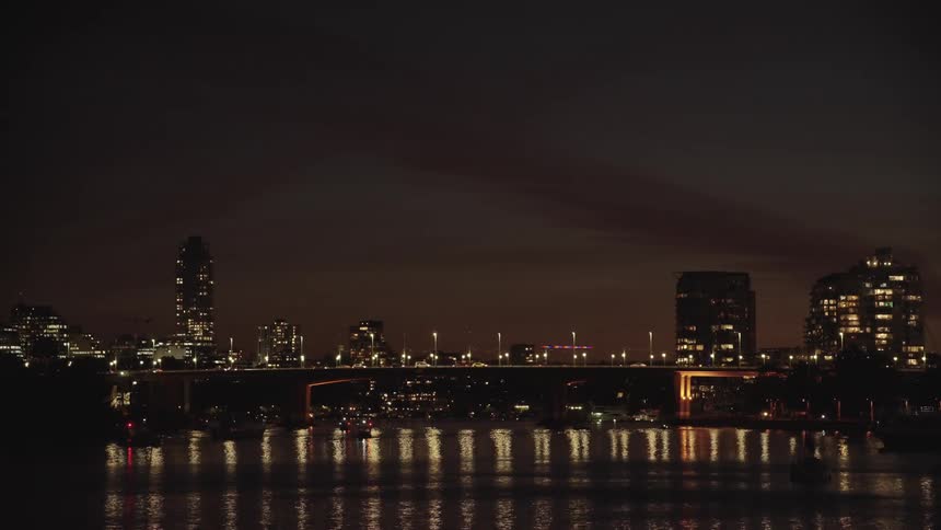 A cityscape with a lit bridge reflecting on the water at night