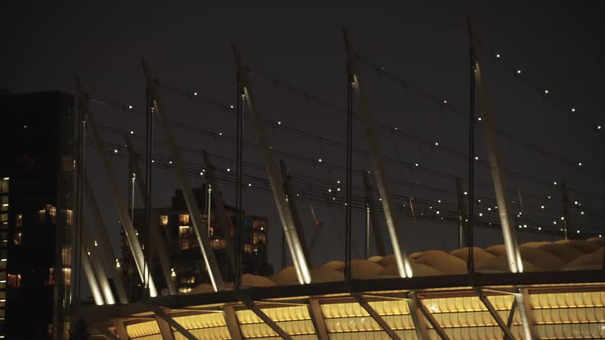 The modern architectural details of a stadium at night with bright lights illuminating the structure against the dark sky