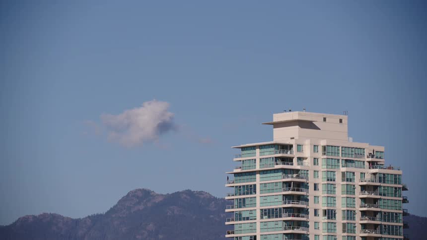 A tall residential building with many balconies set against a bright blue sky with dark angular mountains visible immediately behind the structure
