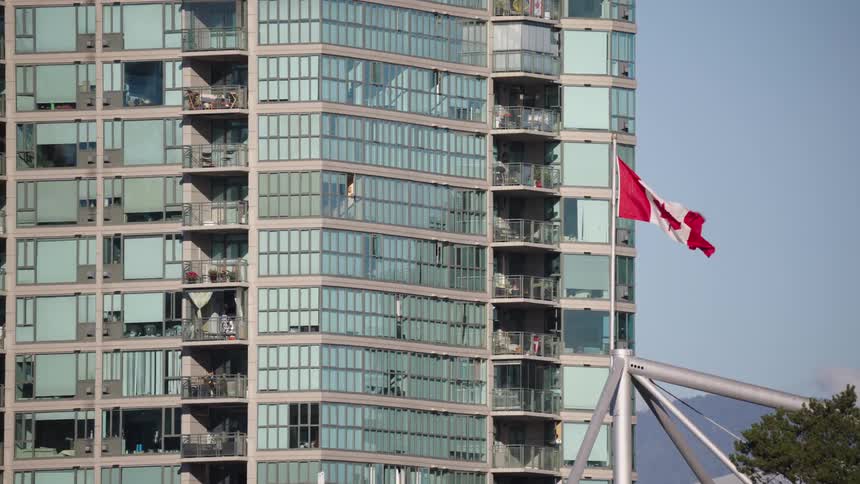 A large multistory structure with a highly segmented glass facade with a rectangular red and white national flag positioned on the right side